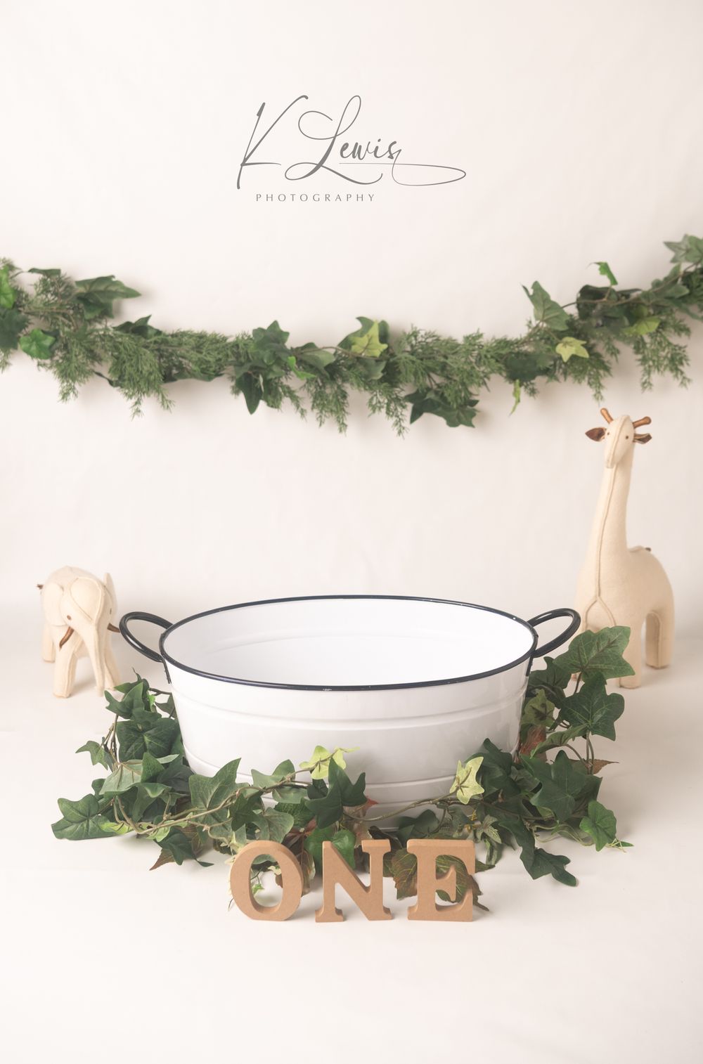 White enamel tub with ivy garland, wooden ONE letters, and giraffe figurines for a first birthday photo session.