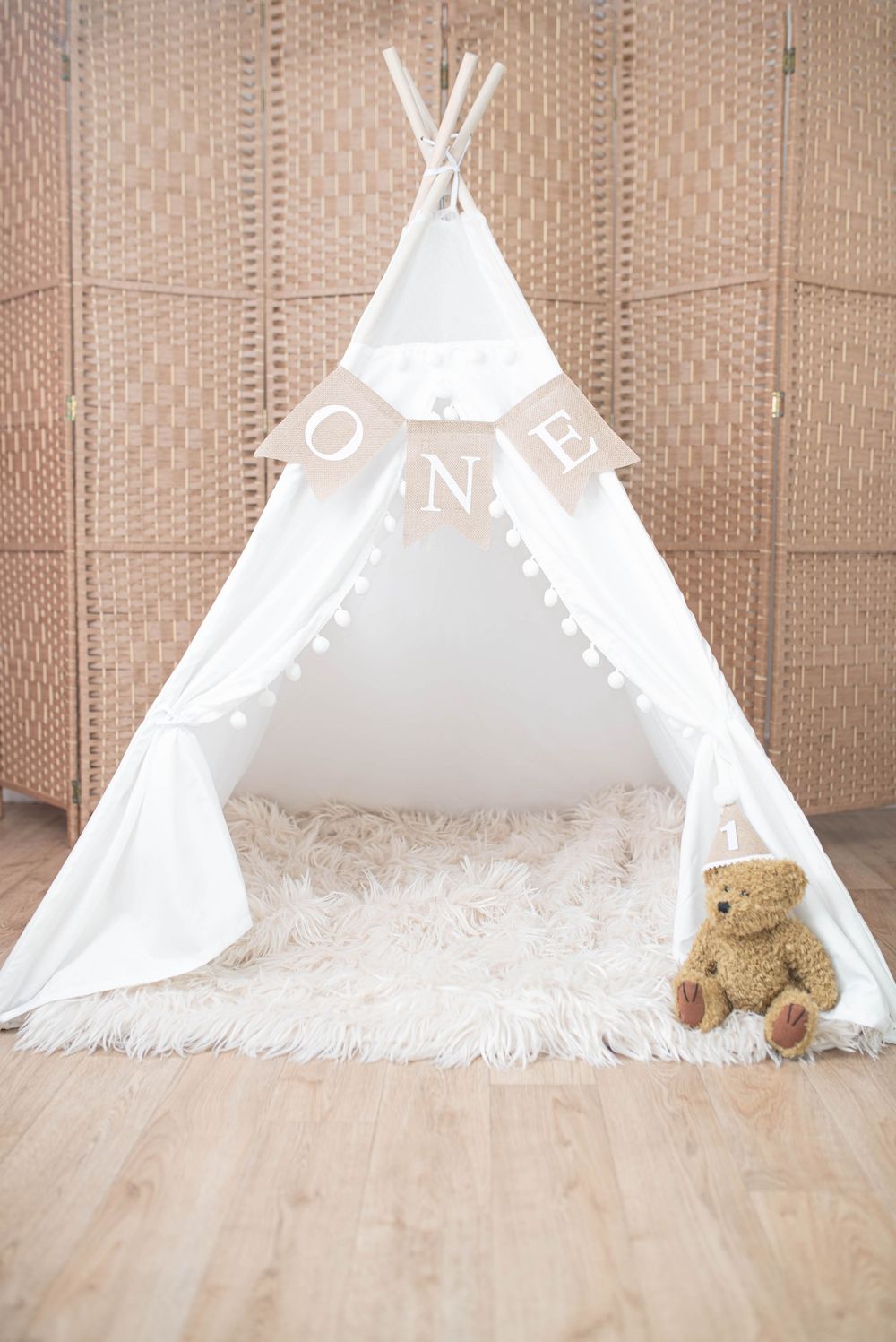 White teepee tent with ONE banner and teddy bear on fluffy rug for first birthday photo shoot.