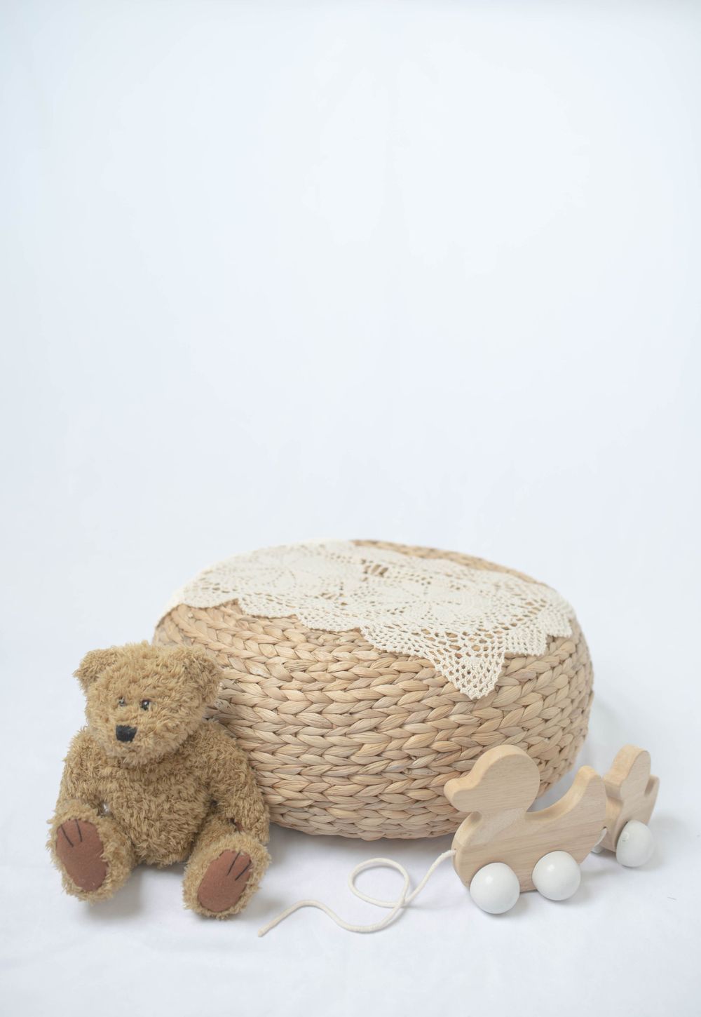 Woven basket with lace doily beside a teddy bear and wooden toy on white background.