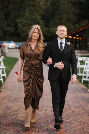 A couple in formal attire walks together on a brick pathway at an outdoor wedding venue with string lights overhead.