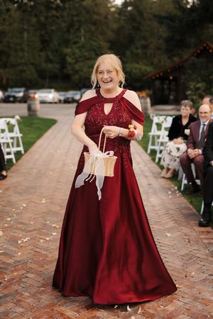 A flower girl in a burgundy dress walks down a brick pathway at an outdoor wedding ceremony, scattering petals.