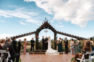 Panoramic view of an outdoor wedding ceremony under a wooden arch with blue skies and white clouds.