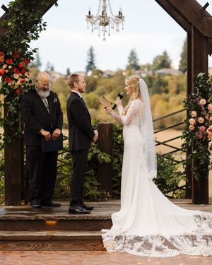 A wedding ceremony takes place under a rustic wooden pavilion decorated with floral arrangements and a crystal chandelier.