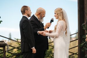 A wedding ceremony takes place outdoors with the couple and officiant standing together during the exchange of vows.