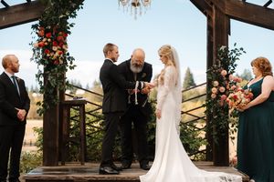 Wedding ceremony takes place under a rustic wooden gazebo decorated with hanging floral arrangements.