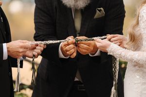 Hands of wedding couple and officiant during traditional ring exchange ceremony at elegant indoor venue.