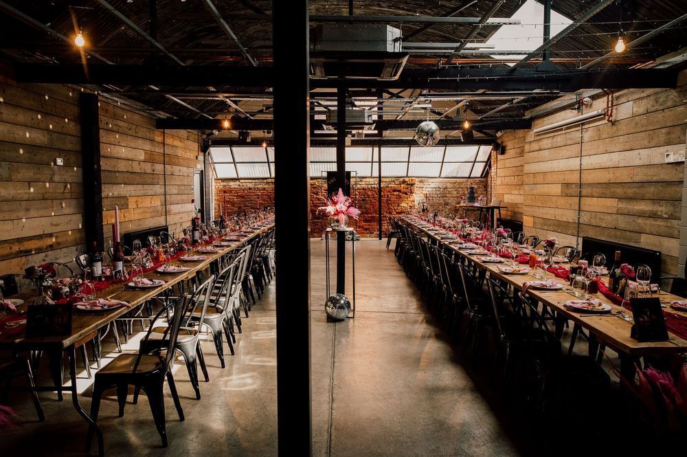 Panoramic view of a rustic industrial event space with wooden walls, exposed beams, and rows of tables and chairs.