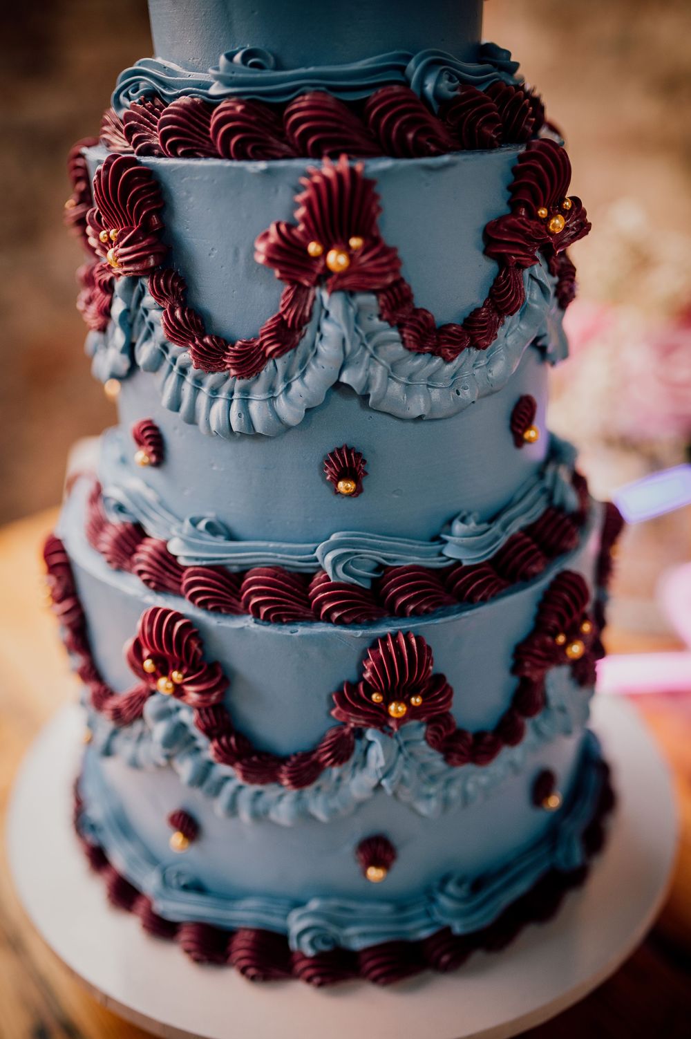 A tiered wedding cake decorated with light blue frosting and burgundy piped details creates an elegant vintage design pattern.