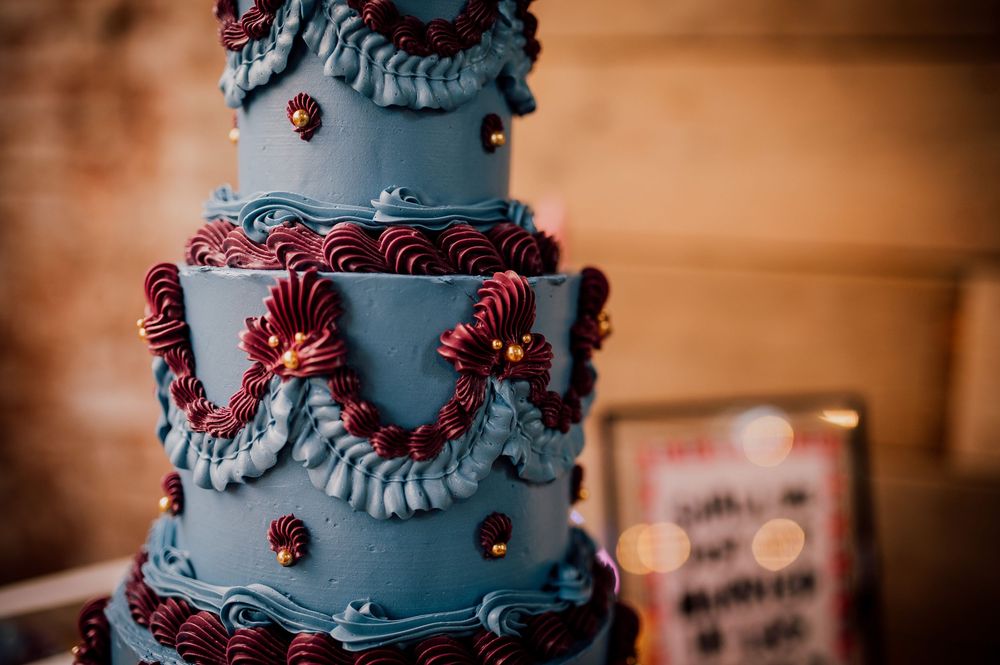 A multi-tiered blue and red wedding cake decorated with intricate ruffles and polka dots on display at a reception.