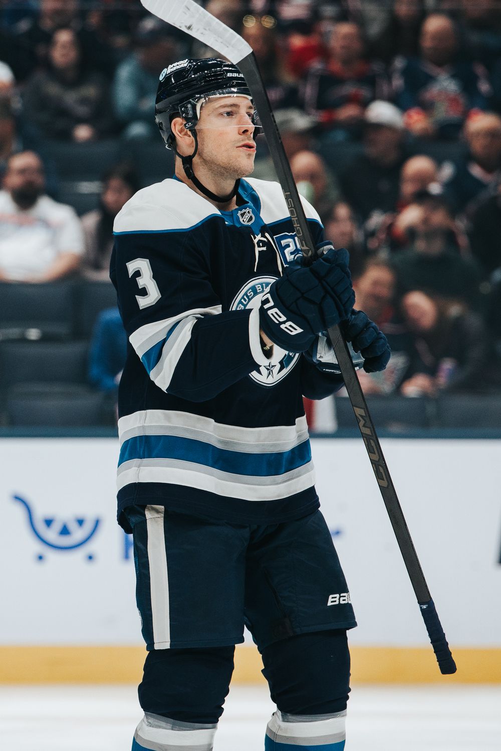 A hockey player in a navy blue and white uniform stands on ice during a game.