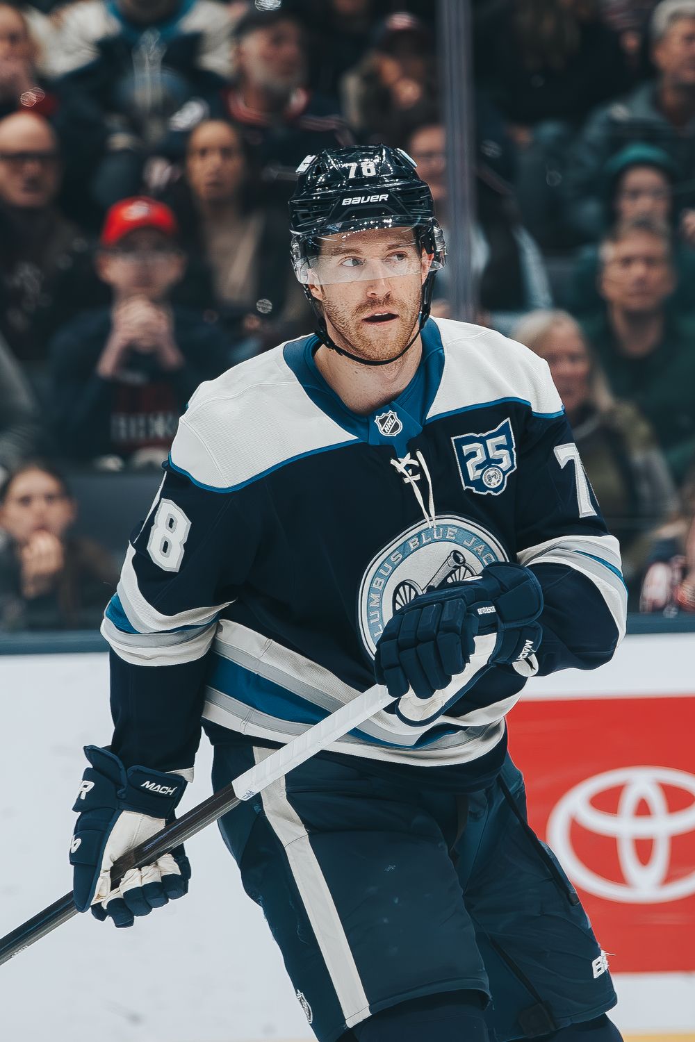 NHL player in a navy and white jersey skates on ice during a professional hockey game.