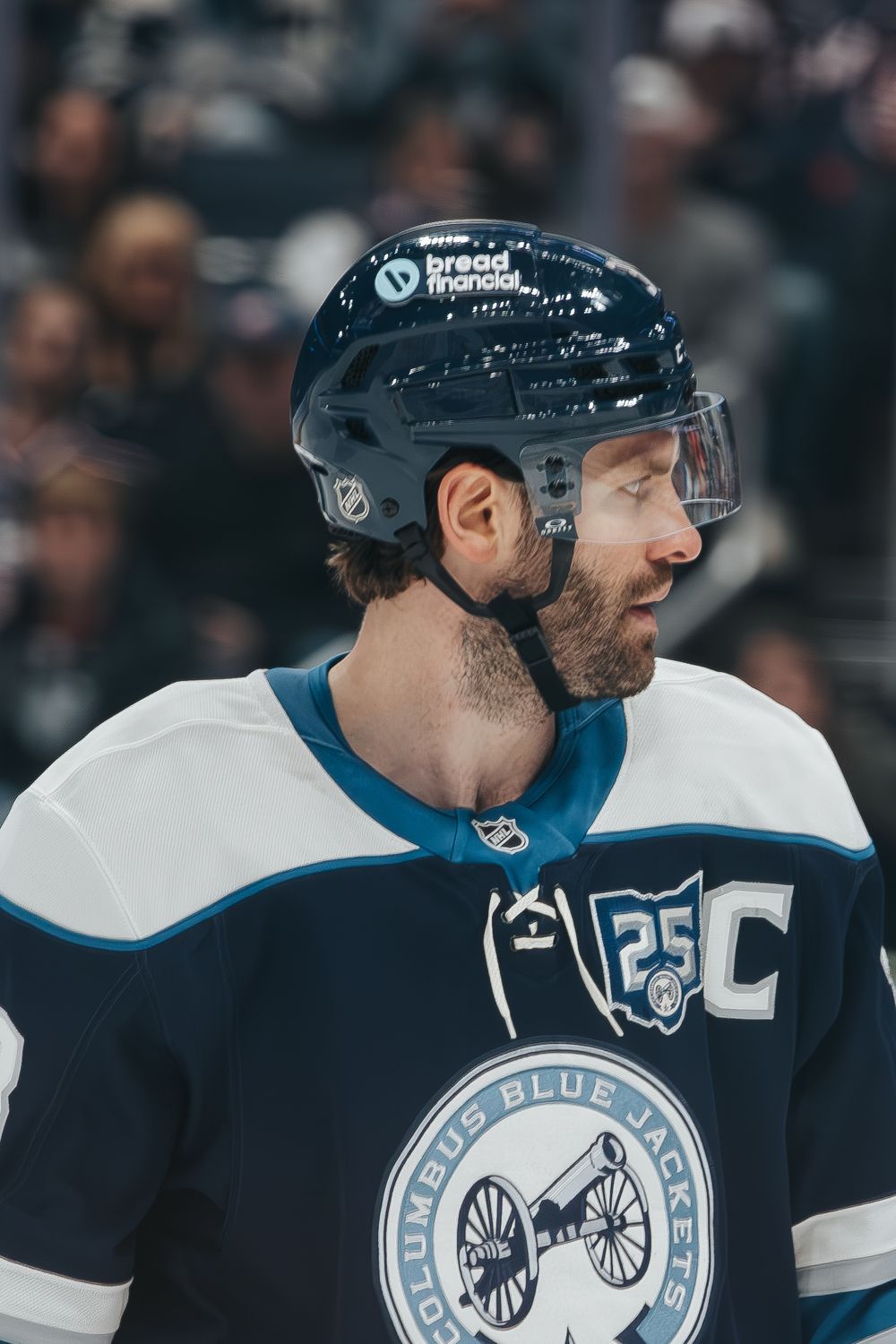 Side profile view of hockey player wearing Columbus Blue Jackets jersey with helmet and visor during game.