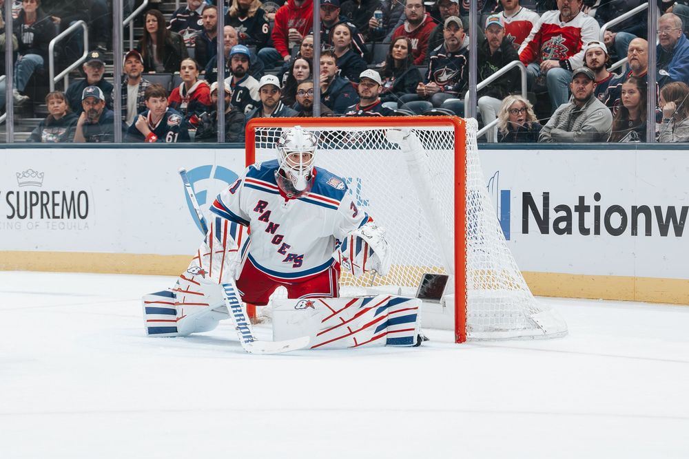 NHL hockey goalie in white and red uniform makes a save during an intense game.