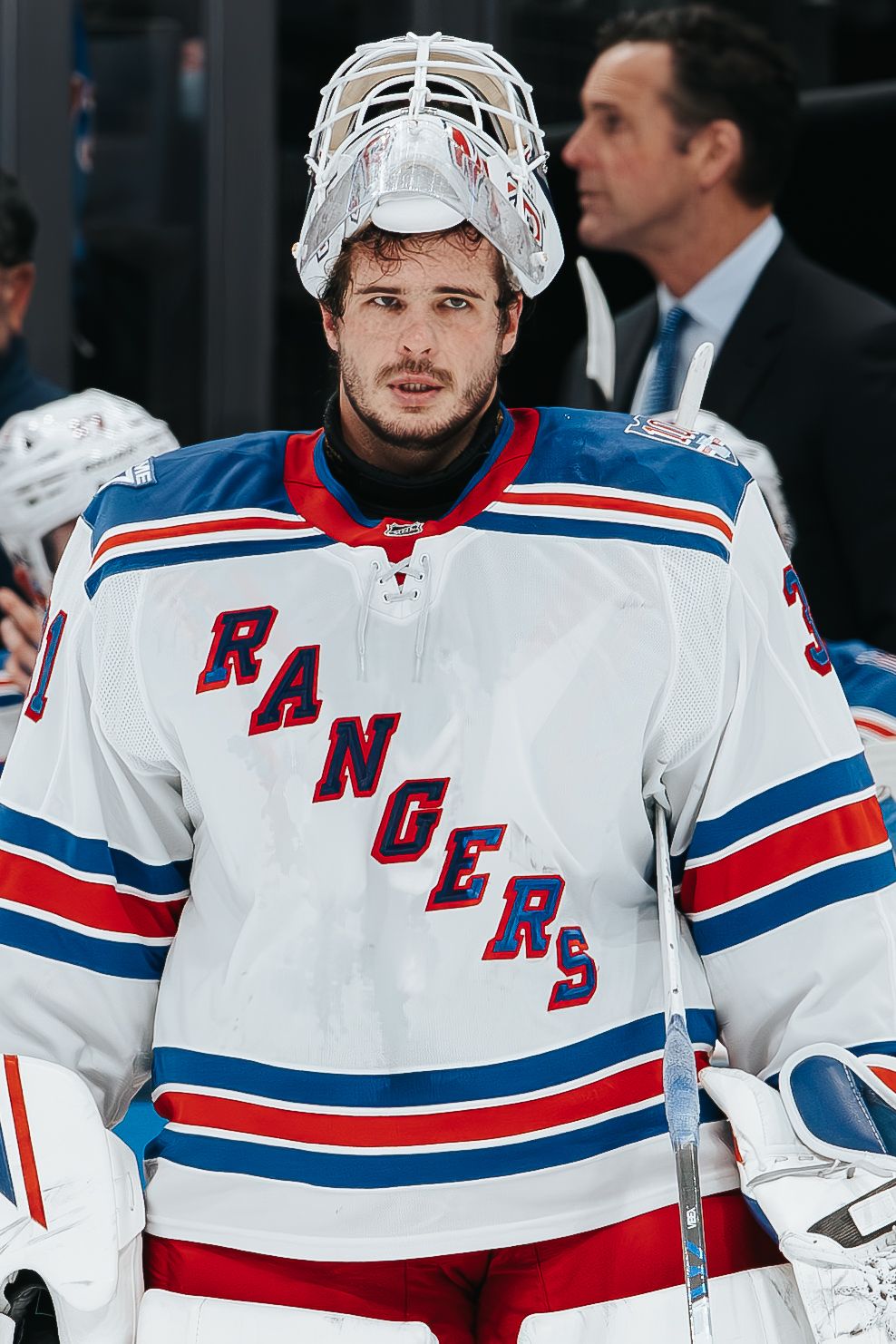 NHL hockey players in New York Rangers white jerseys with red and blue trim stand together on the ice during a game.