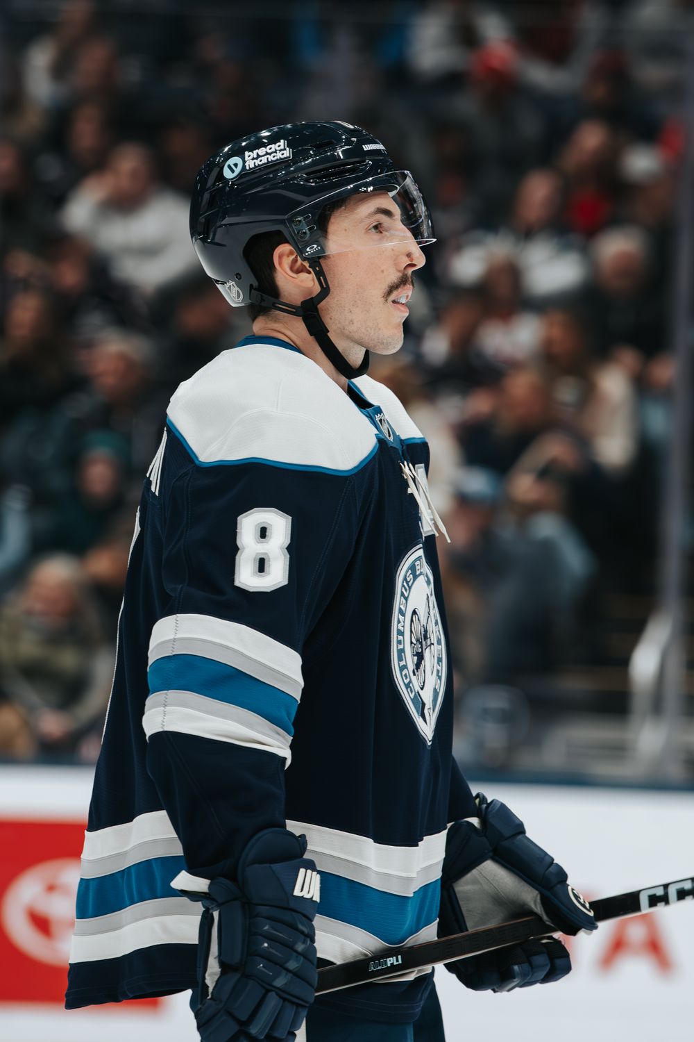 Hockey player wearing a dark blue and white jersey with number 8 skating on ice during a game.