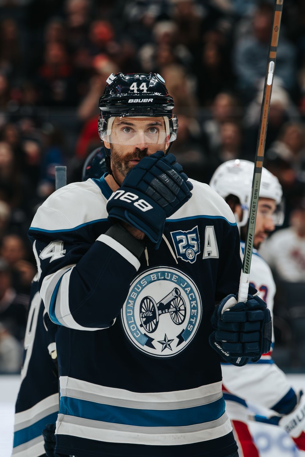 A hockey player wearing a Columbus Blue Jackets 25th anniversary jersey looks up during a game.