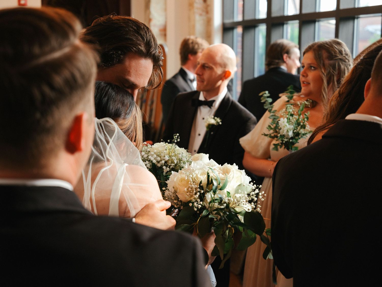 Candid reception moment captured with guests mingling in natural window light.