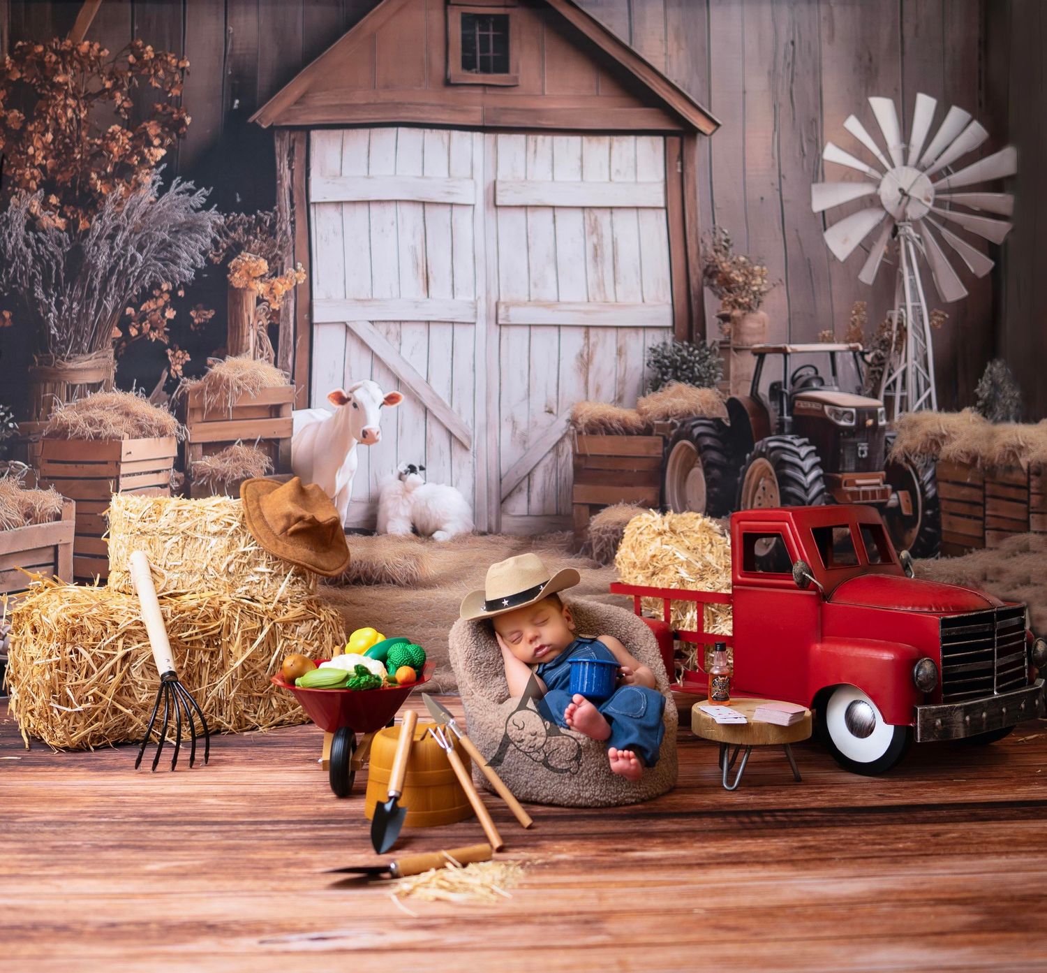 Baby in farmer hat sits in burlap sack on hay bale with red truck, barn, goats, and farm tools in rustic photo backdrop.