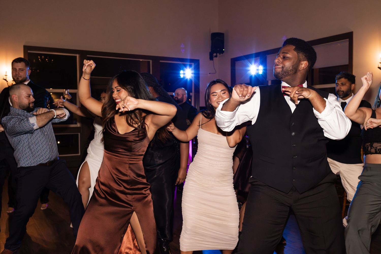 Guests dance enthusiastically at a wedding reception with blue lighting in the background.