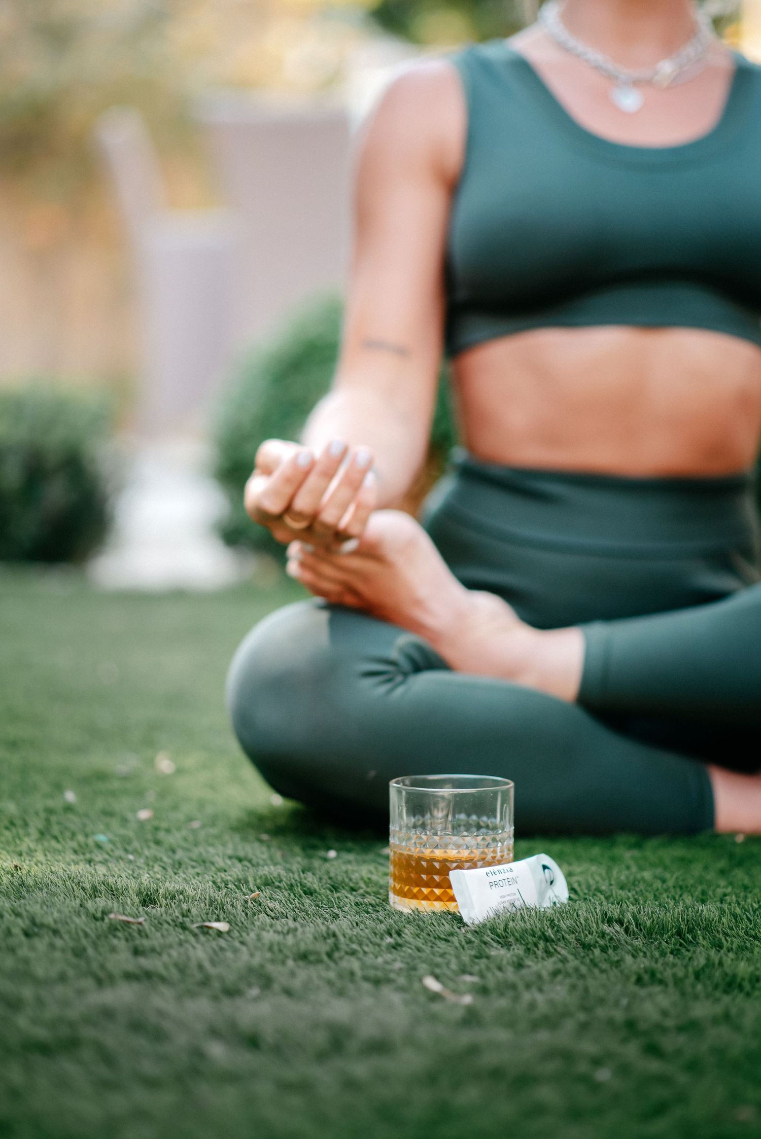lifestyle photography of a woman sitting crossed legged on the grass with a sachet of supplement next to her.