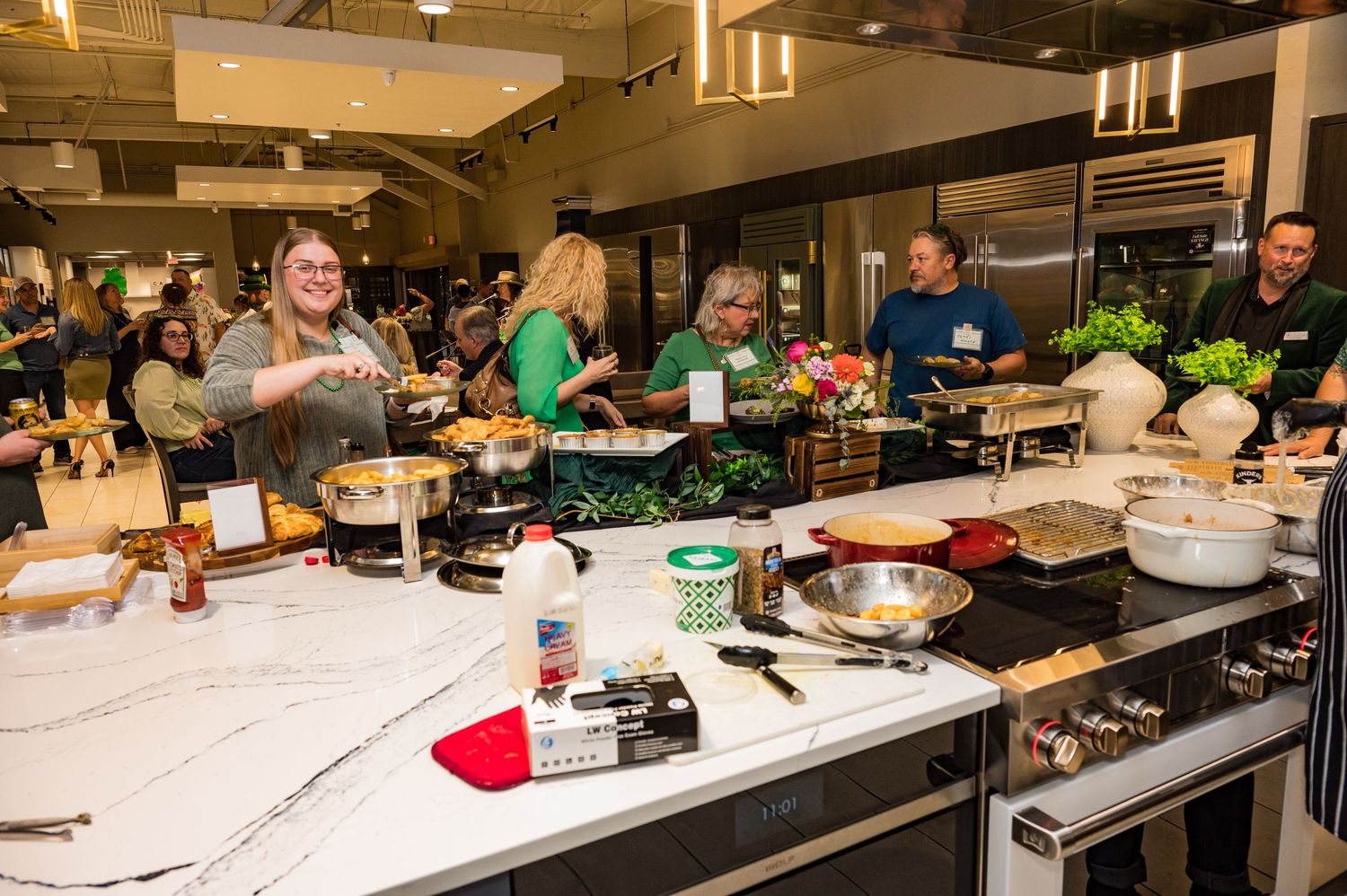 Guests and staff cooking together at a busy kitchen island during a St. Patricks Day culinary event.