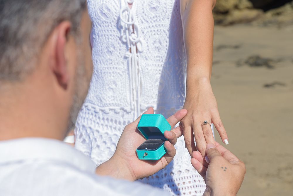 Close-up of a turquoise ring box and white lace dress during a beach proposal.