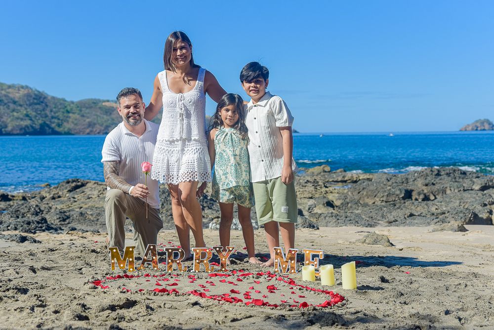 Family gathering on a rocky beach shoreline with mountains and ocean in the background.