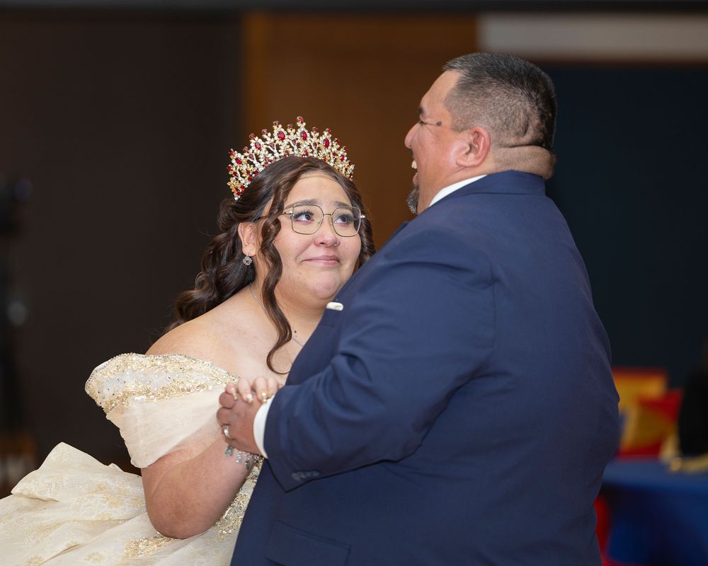 A couple shares their first dance at a wedding reception, with the bride wearing a white gown and groom in navy suit.