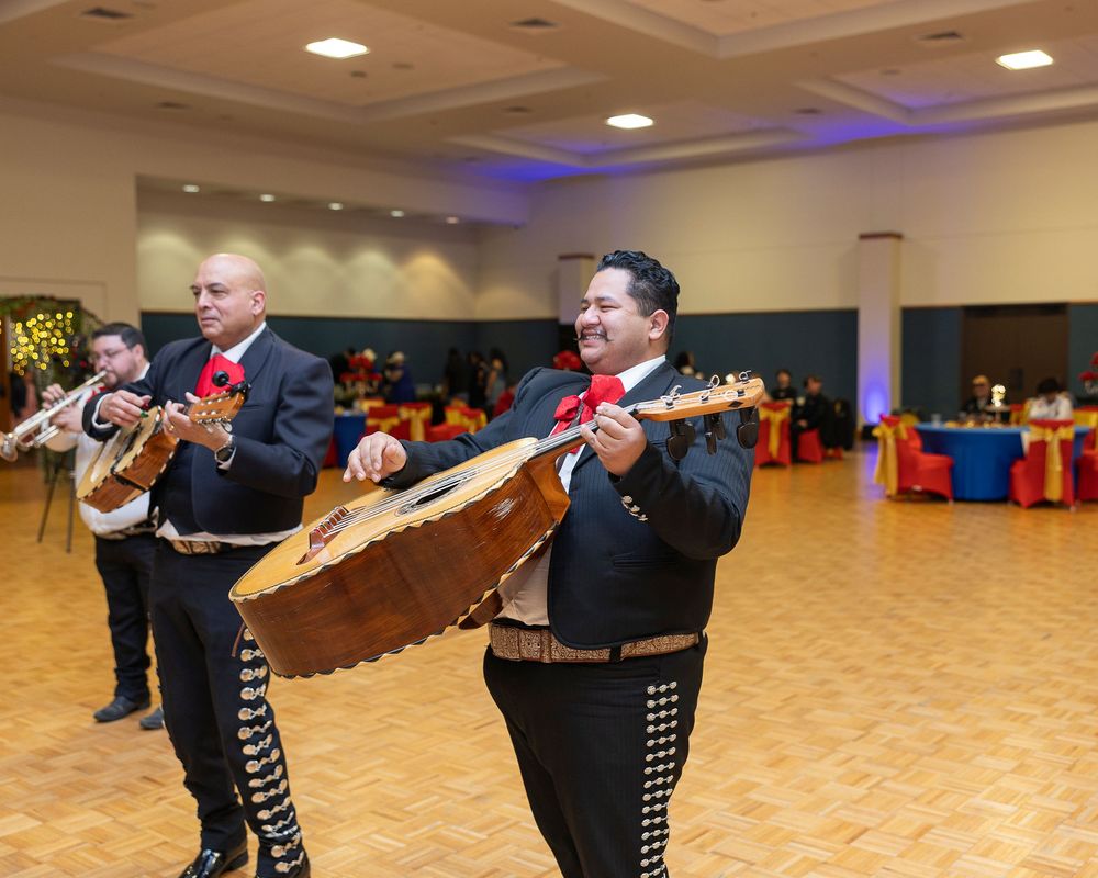 Traditional Mexican mariachi musicians perform in a dance hall with wooden floors and recessed lighting.