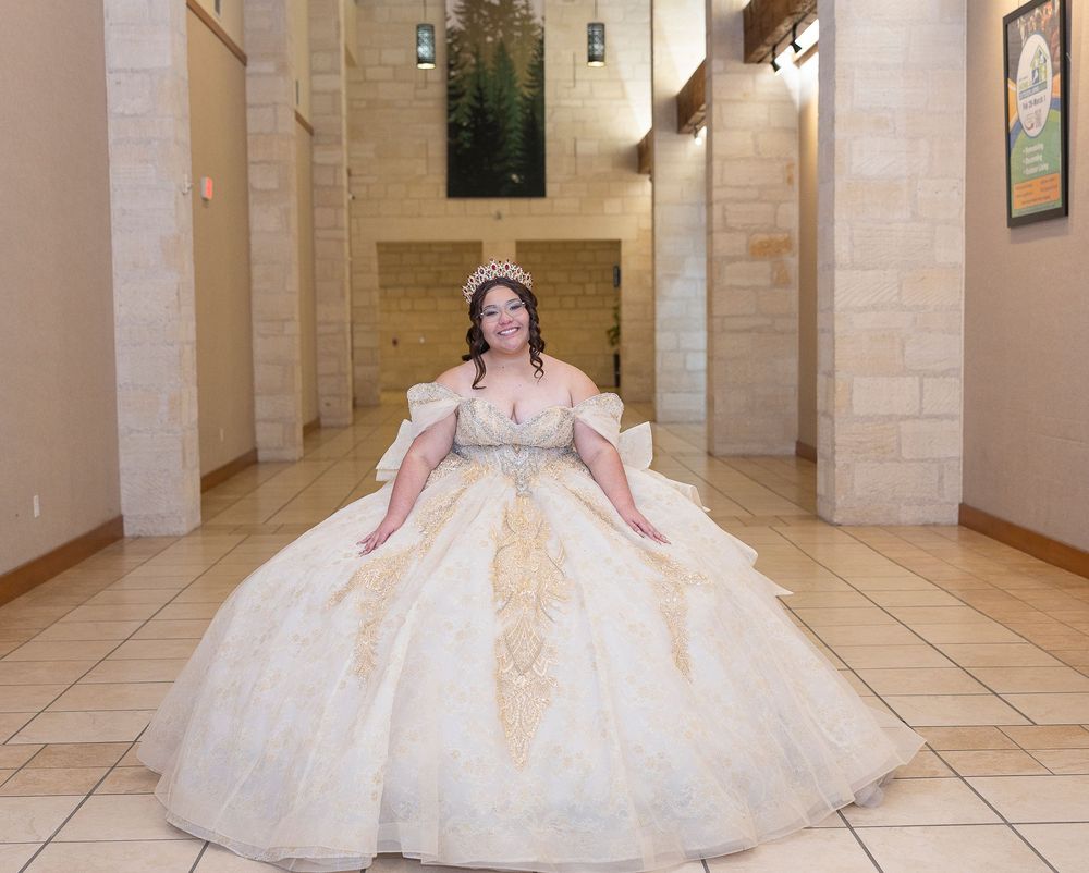 A bride in an elegant cream ballgown twirls in a marble-floored hallway with classical architectural details.