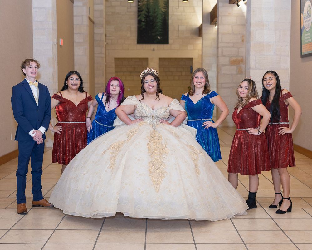 Wedding party members in blue suits and burgundy dresses pose playfully on a light tile floor in a reception venue.