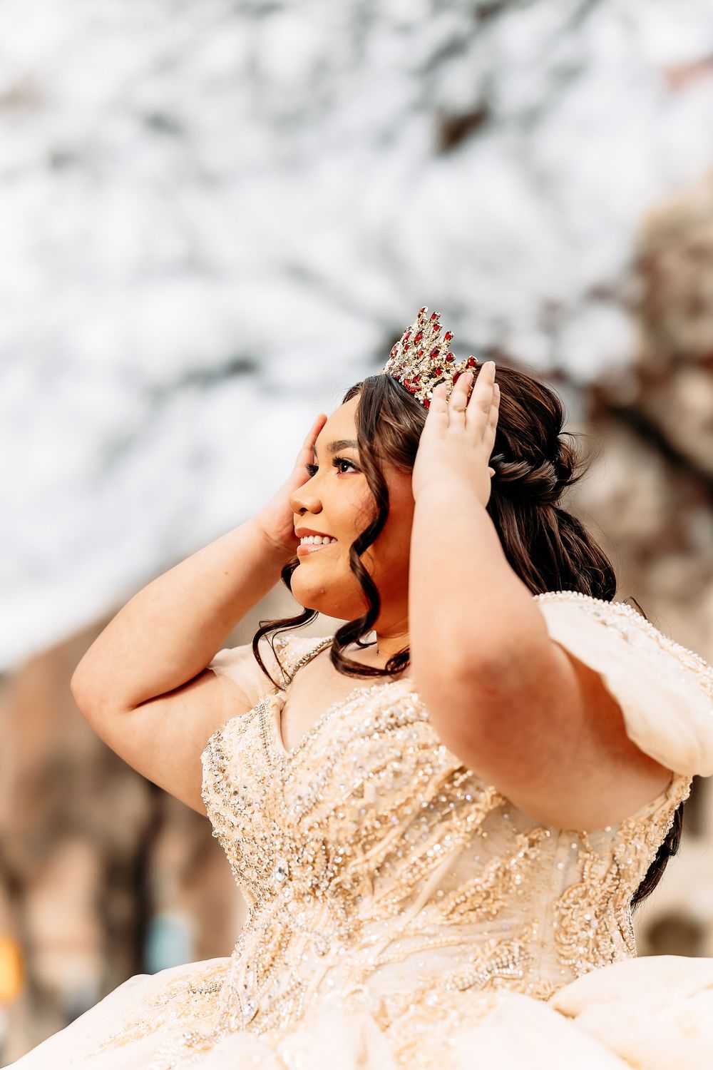 A close-up portrait showing a sparkling cream-colored gown and delicate crown against a soft blurred background.