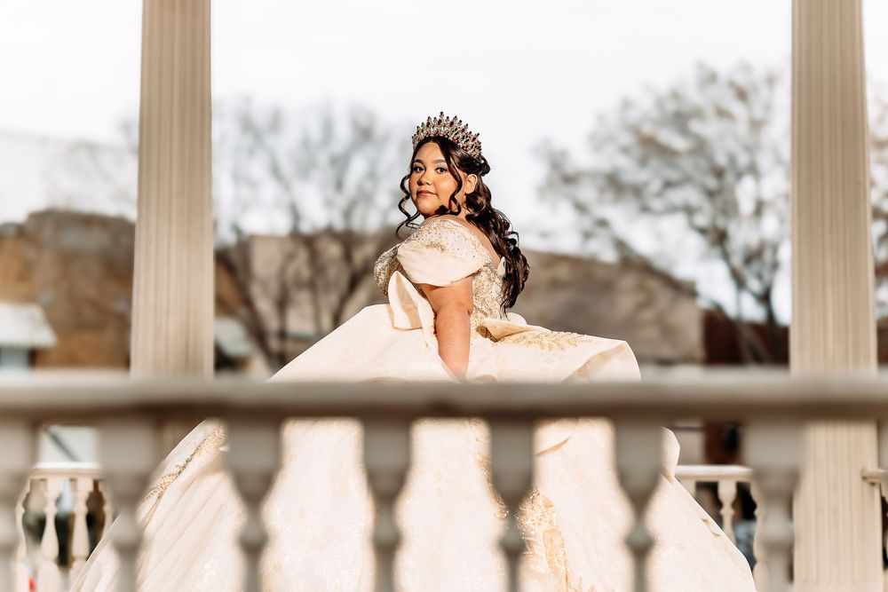 A bride in an elegant white gown poses on a balcony with classical columns in the background.
