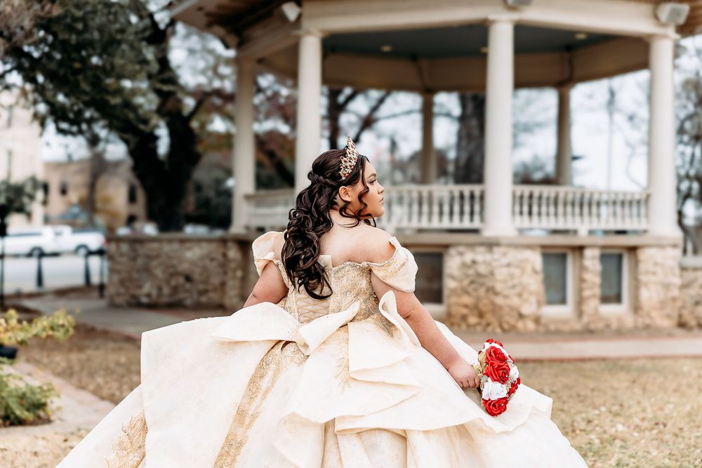 A bride in a flowing white ballgown poses in a rustic outdoor setting with stone columns and greenery.