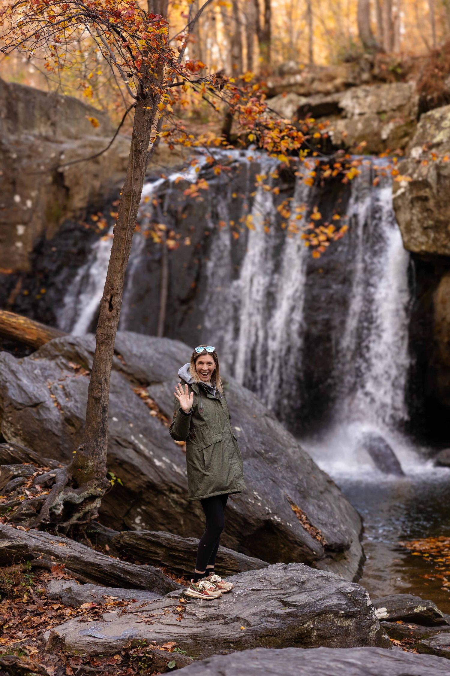 Scenic autumn waterfall cascades down rocky cliffs surrounded by golden fall foliage in a peaceful forest setting.