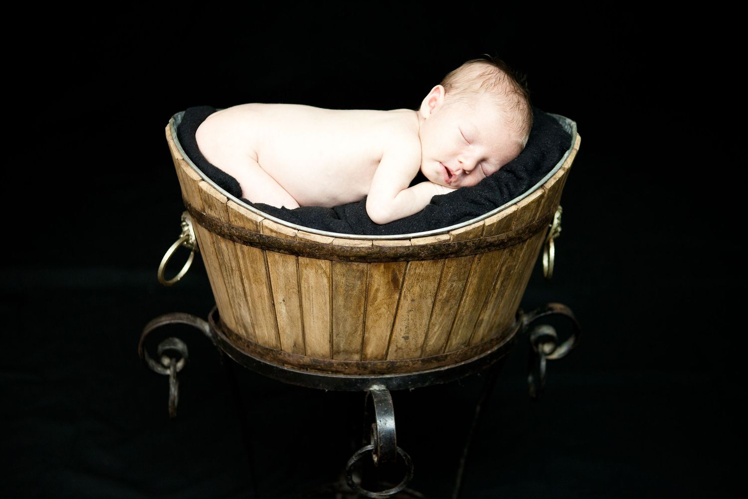 A series of photos showing a sleeping baby nestled in a rustic wooden basket against a dark background.