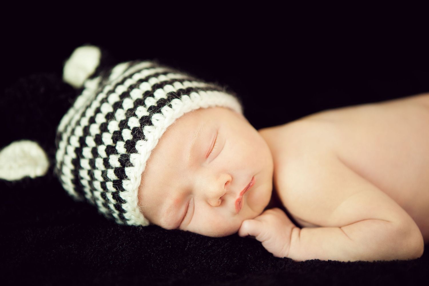 A series of black and white photographs showing a baby's hands and feet wearing a striped knit hat.