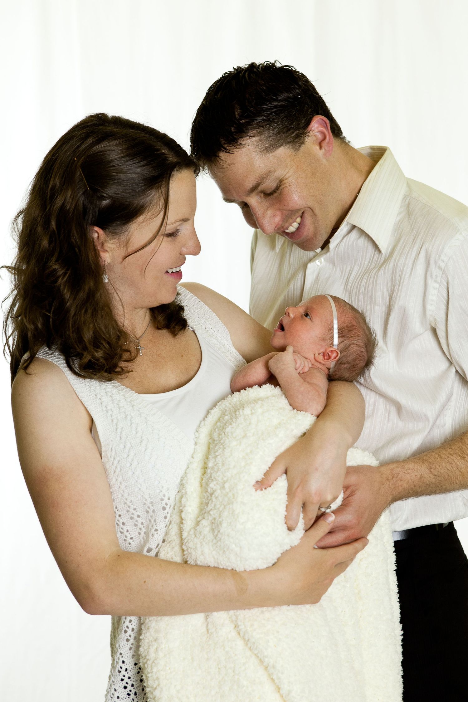A series of tender moments showing parents cradling and bonding with their newborn baby in white clothing.