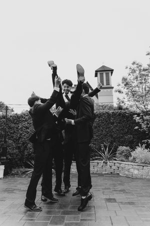 Groomsmen lifting groom in the air outdoors in black and white wedding photo.