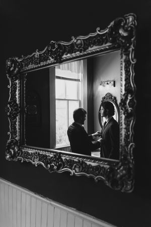 Black and white mirror reflection of two men in suits preparing for a wedding ceremony.