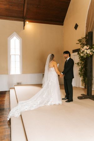 Bride and groom holding hands at the altar of a white chapel during their wedding ceremony.
