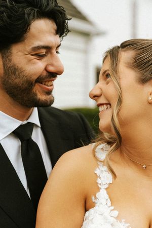 Happy bride and groom in wedding attire smile at each other in a close romantic outdoor portrait.