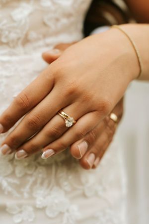 Close-up of a bride's hand wearing a gold diamond solitaire engagement ring and wedding band with French tip nails.