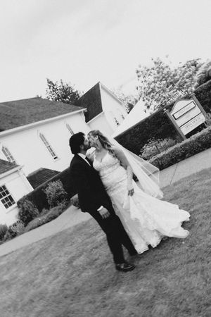 Black and white photo of a bride and groom sharing a kiss outside a white church on their wedding day.