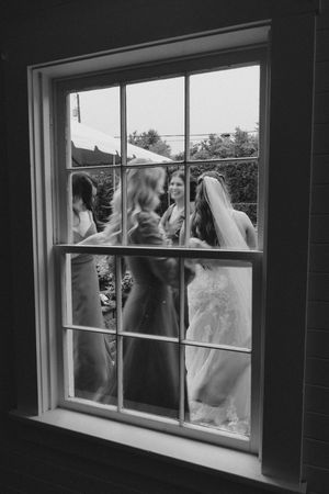 Black and white photo of bride in veil with bridesmaids seen through vintage window panes.