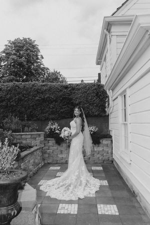 Elegant bride in lace wedding gown with long train and veil posing in garden in black and white photo.