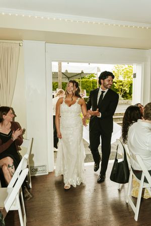 Bride and groom make grand entrance at wedding reception, guests applauding as couple walks through doorway.