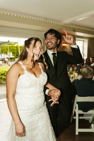 Joyful bride in lace gown and groom in black suit celebrate at their wedding reception venue.