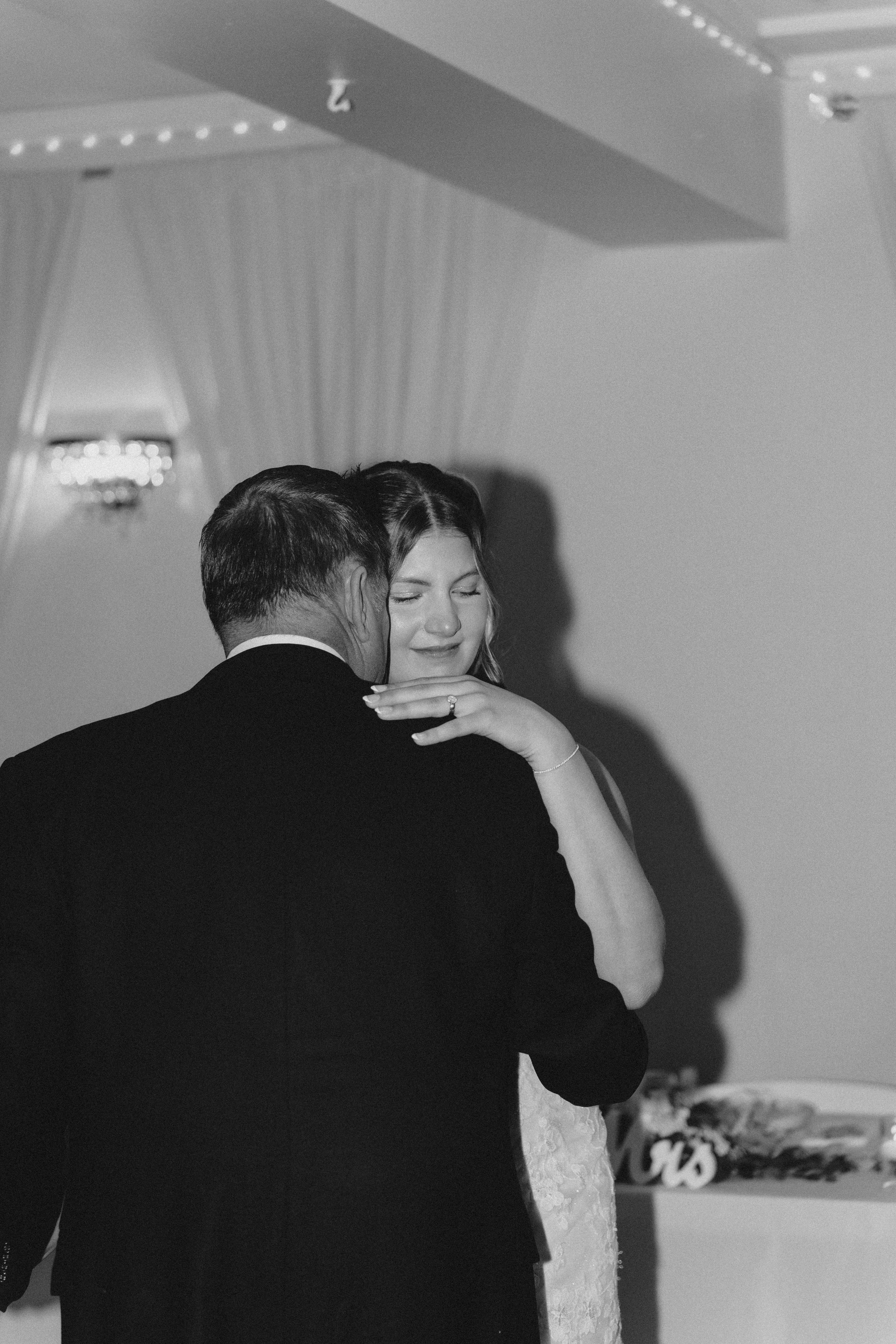 Black and white photo of emotional bride dancing with groom at wedding reception, eyes closed, smiling tenderly.