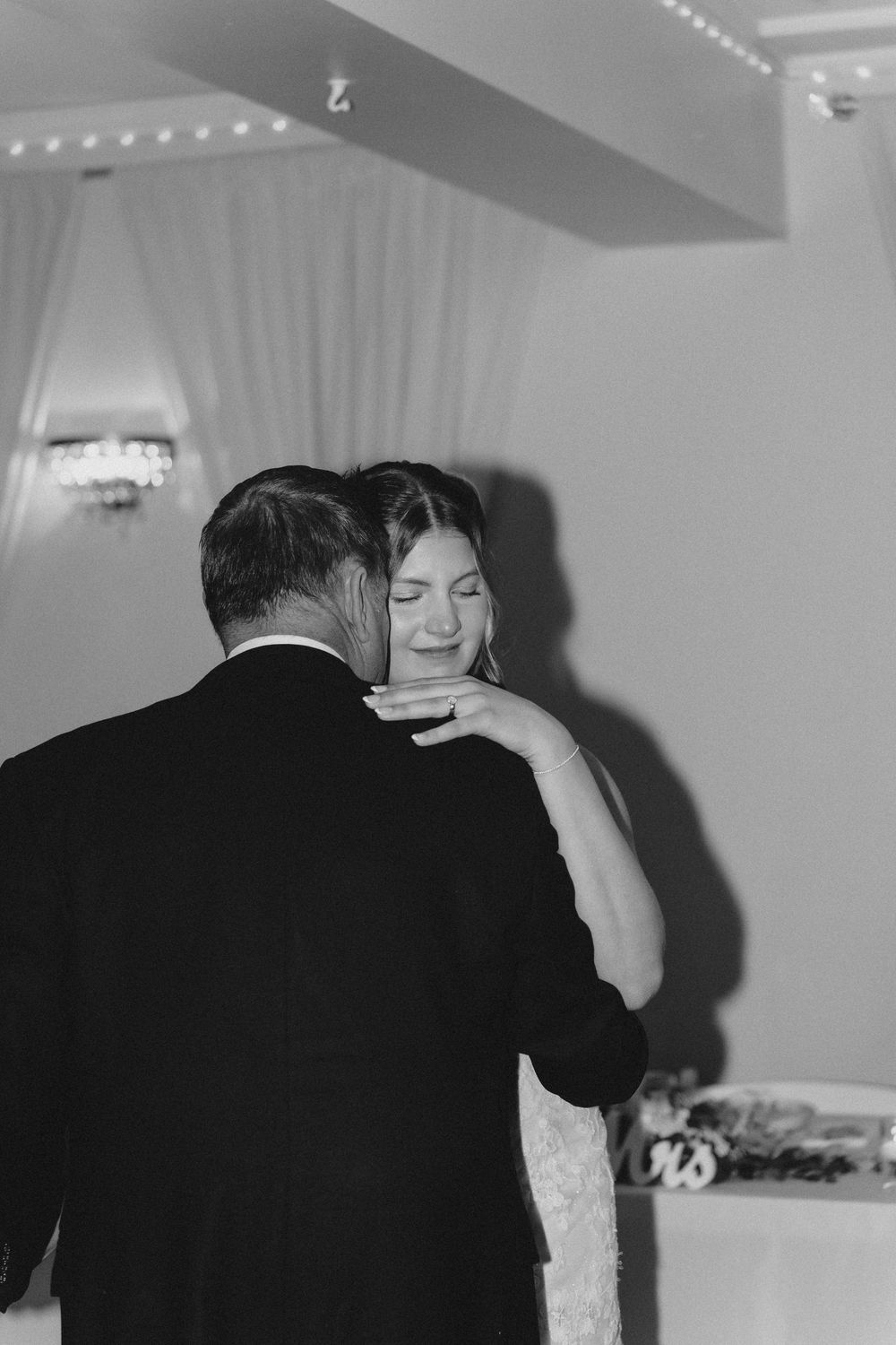 Black and white photo of emotional bride dancing with groom at wedding reception, eyes closed, smiling tenderly.